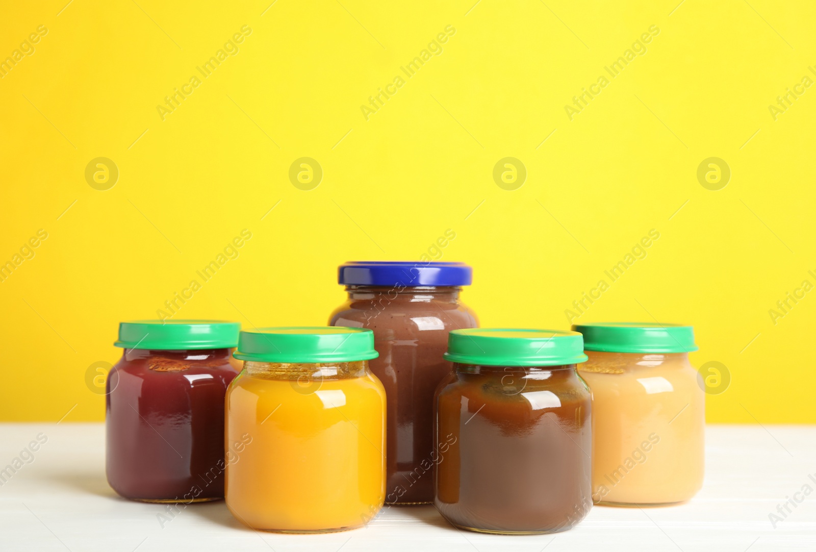 Photo of Jars with baby food on white wooden table against yellow background