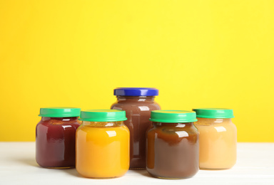 Jars with baby food on white wooden table against yellow background