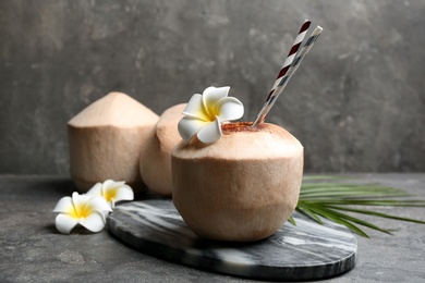 Photo of Young peeled coconuts with straw, palm leaf and beautiful flowers on grey table