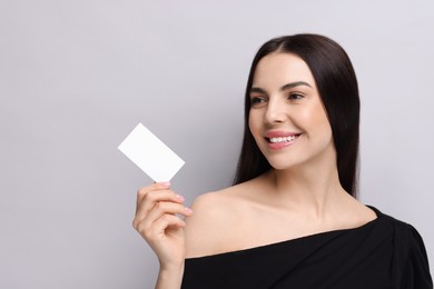 Photo of Happy woman holding blank business card on light grey background. Space for text