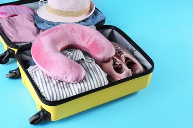 Photo of Opened suitcase with travel pillow and clothes on light blue background, above view