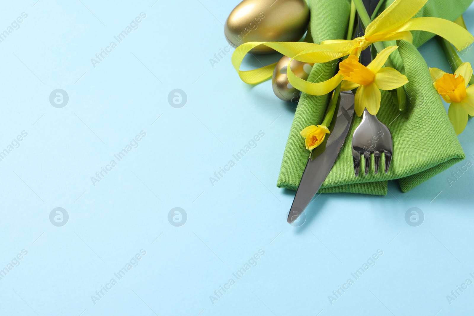 Photo of Cutlery set, Easter eggs and narcissuses on light blue background, space for text. Festive table setting