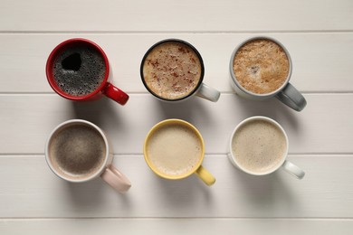 Many cups with different aromatic coffee on white wooden table, flat lay