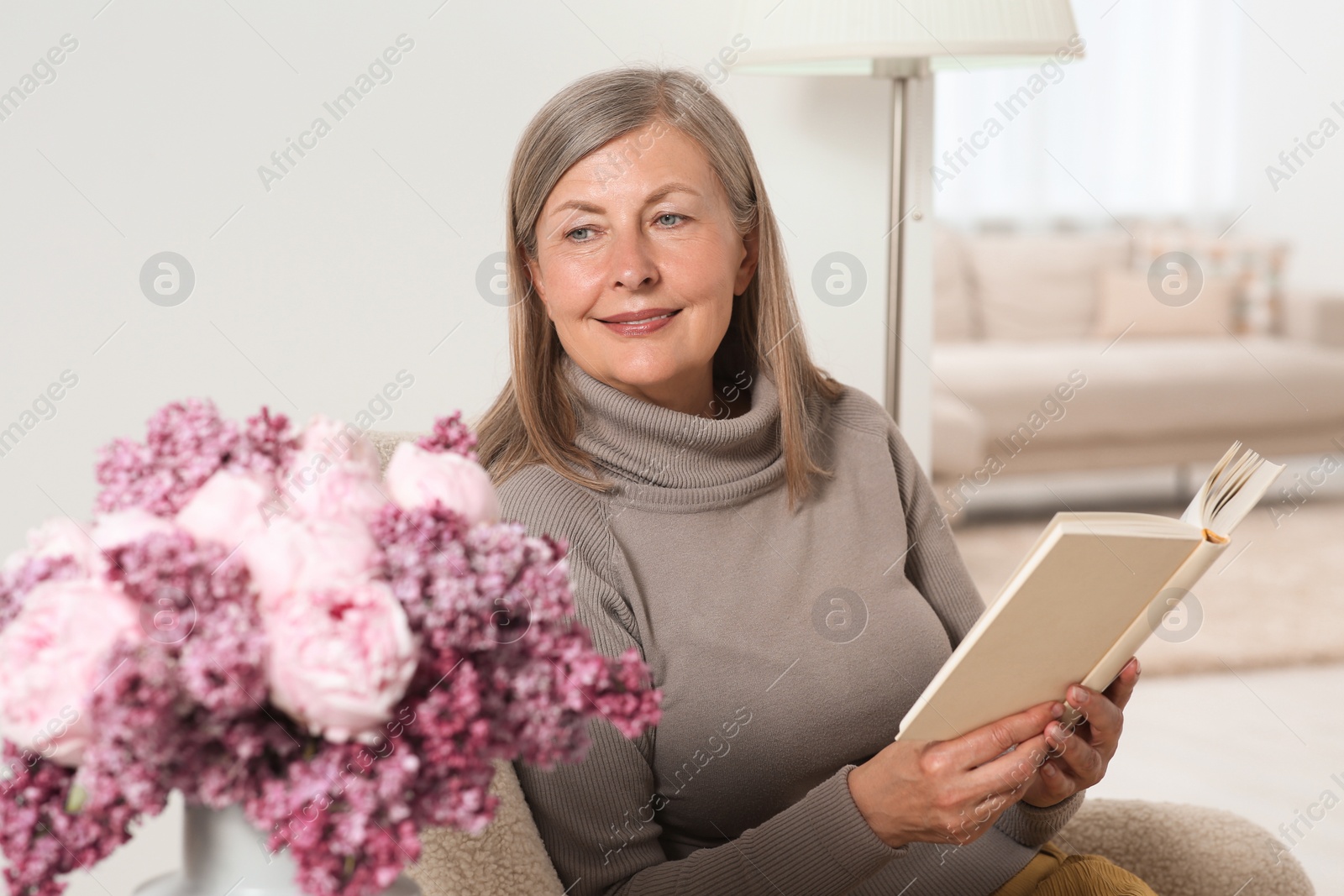 Photo of Beautiful senior woman reading book in armchair at home