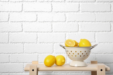Photo of Colander with ripe lemons on table against brick wall