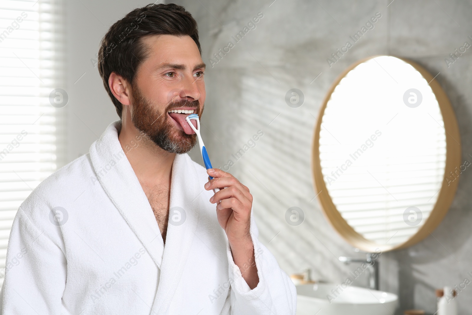 Photo of Happy man brushing his tongue with cleaner in bathroom, space for text