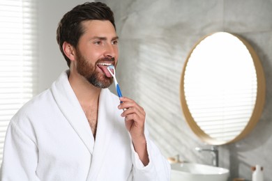 Photo of Happy man brushing his tongue with cleaner in bathroom, space for text