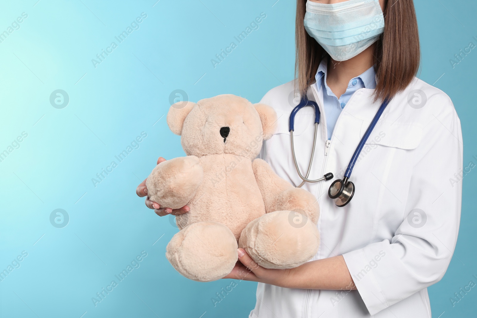 Photo of Pediatrician with teddy bear and stethoscope on light blue background, closeup