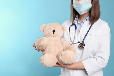 Pediatrician with teddy bear and stethoscope on light blue background, closeup