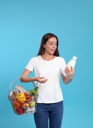 Young woman with shopping basket full of products on blue background