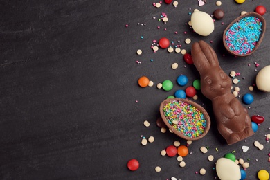 Photo of Flat lay composition with chocolate Easter bunny, eggs and candies on black table. Space for text