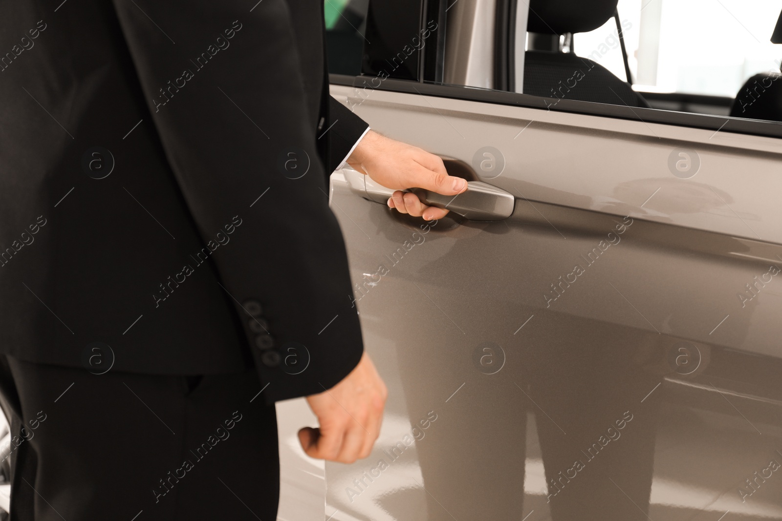 Photo of Young salesman in suit opening car door, closeup view