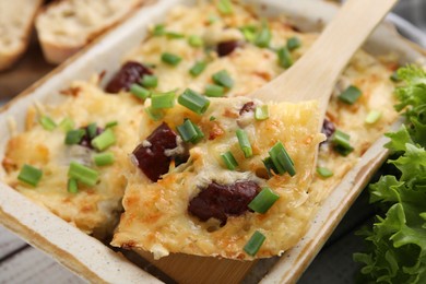 Photo of Taking piece of tasty sausage casserole from baking dish at white table, closeup