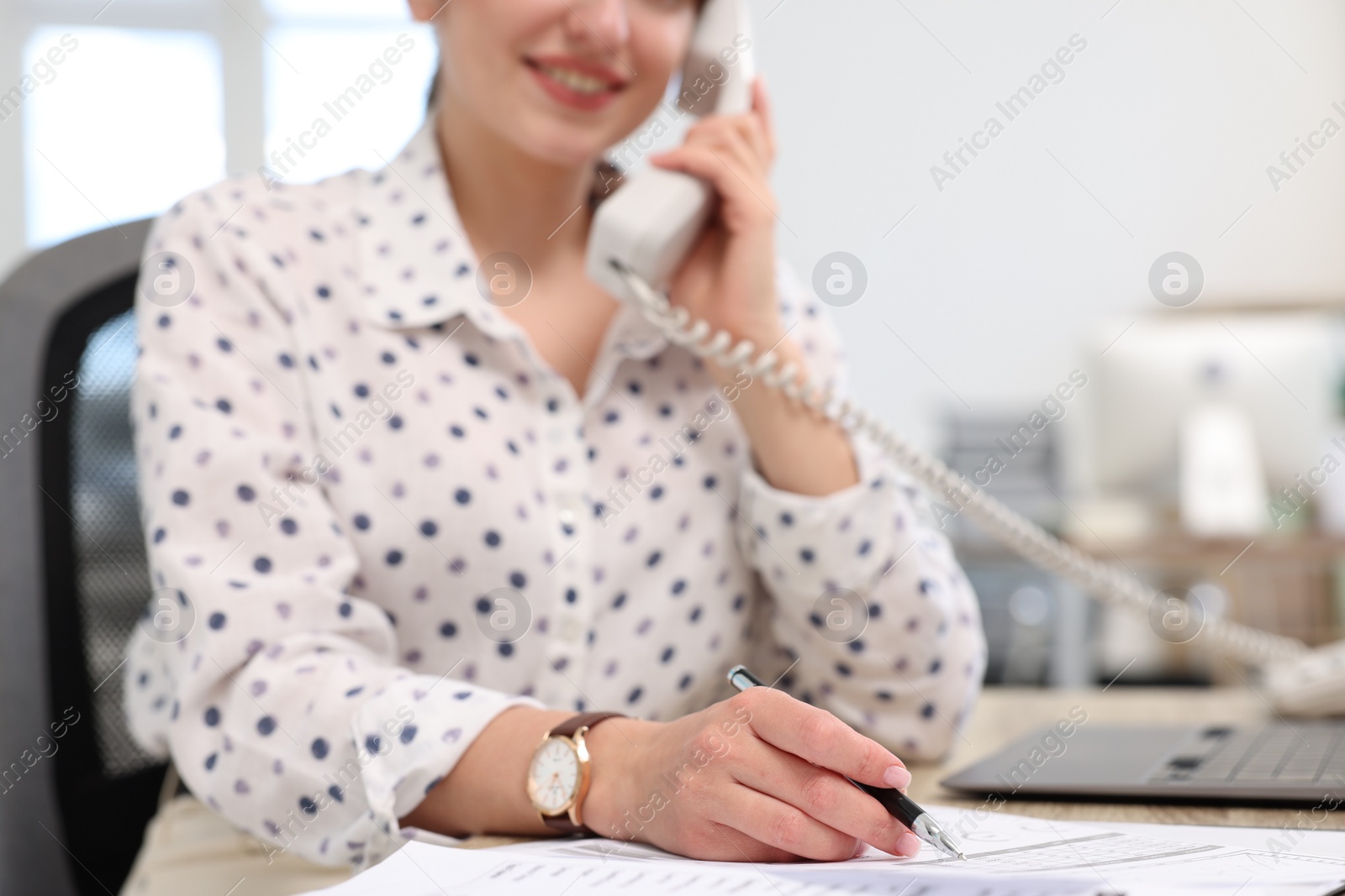 Photo of Smiling secretary talking on telephone at table in office, closeup