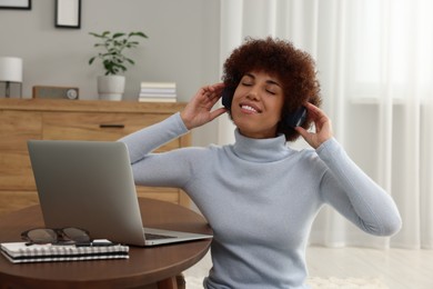 Beautiful young woman in headphones using laptop at wooden coffee table in room