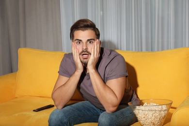 Photo of Emotional man watching with popcorn TV on couch in living room