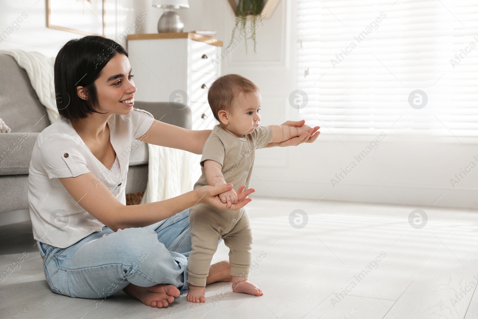 Photo of Mother supporting her baby daughter while she learning to walk at home. Space for text