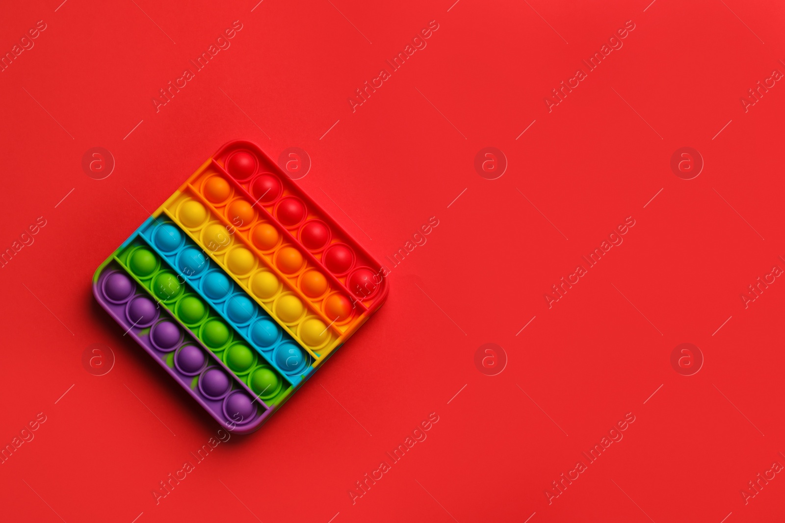 Photo of Rainbow pop it fidget toy on red background, top view. Space for text