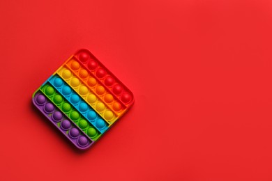 Rainbow pop it fidget toy on red background, top view. Space for text