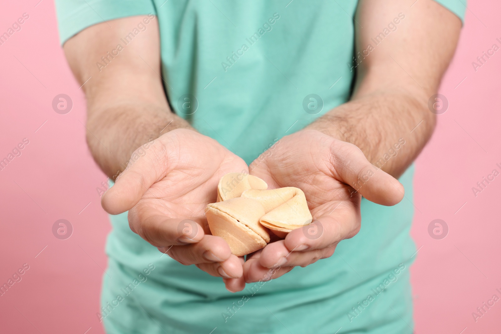 Photo of Man holding tasty fortune cookies with predictions on pink background, closeup