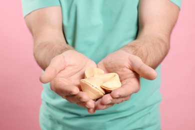 Man holding tasty fortune cookies with predictions on pink background, closeup