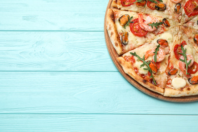 Delicious seafood pizza on light blue wooden table, top view. Space for text