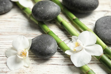 Photo of Bamboo branches, spa stones and flowers on wooden background