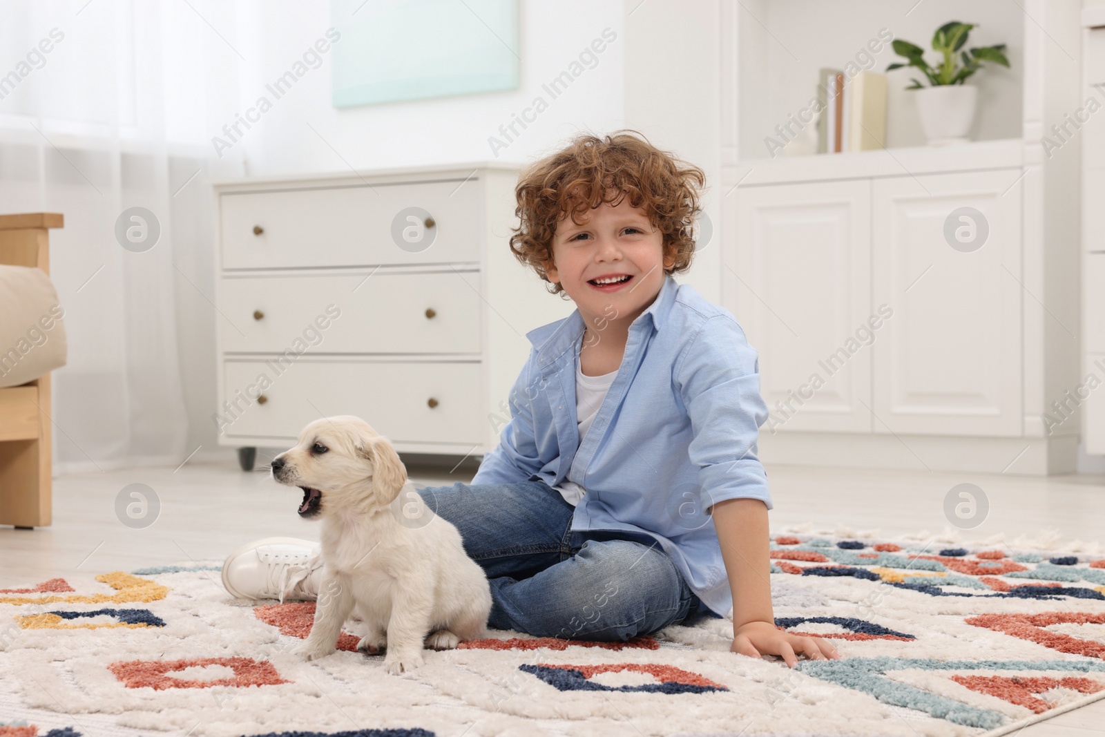 Photo of Little boy with cute puppy on carpet at home