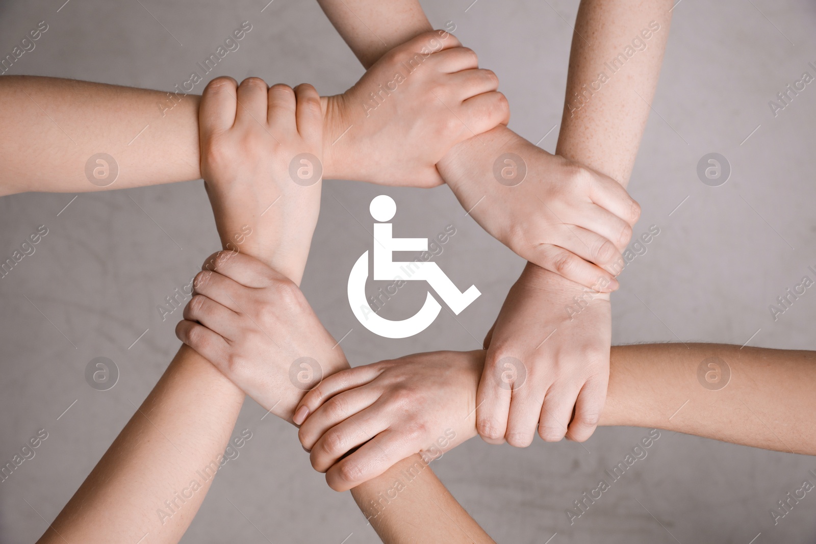 Image of Inclusion concept. People holding hands together around international symbol of access together on grey background, top view