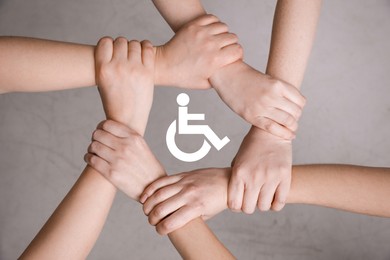 Inclusion concept. People holding hands together around international symbol of access together on grey background, top view