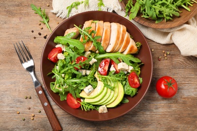 Photo of Delicious salad with chicken, arugula and avocado on wooden table, flat lay