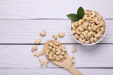 Tasty cashew nuts and green leaves on white wooden table, flat lay