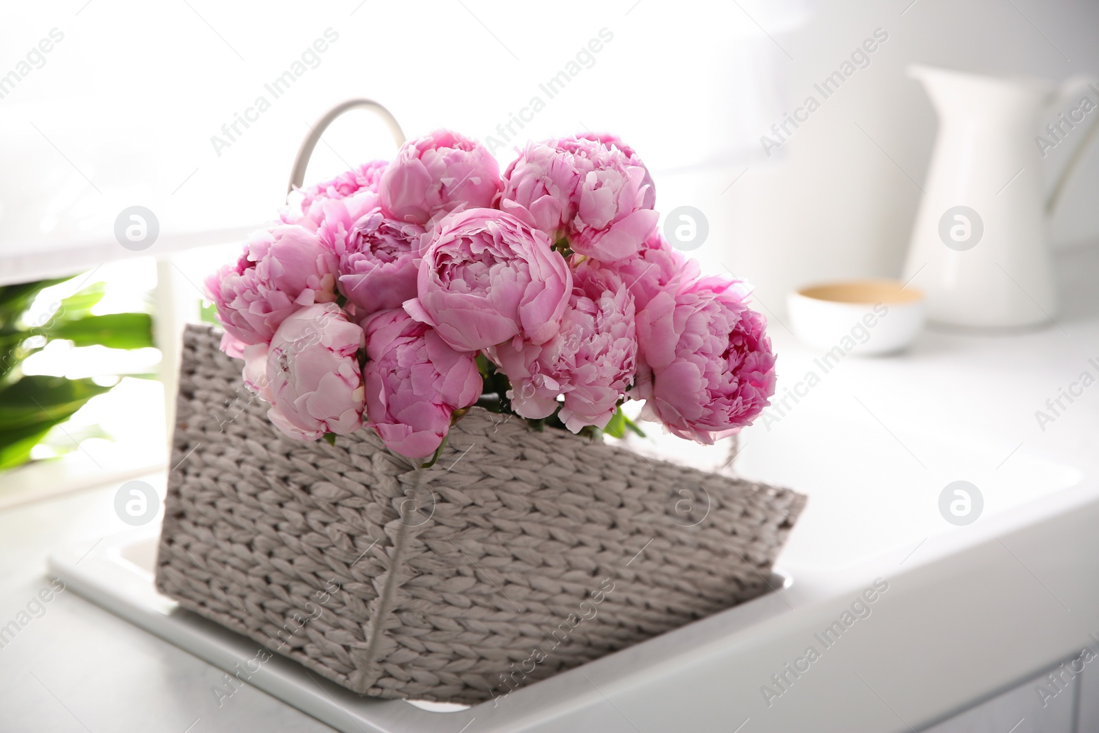 Photo of Basket with beautiful pink peonies in kitchen