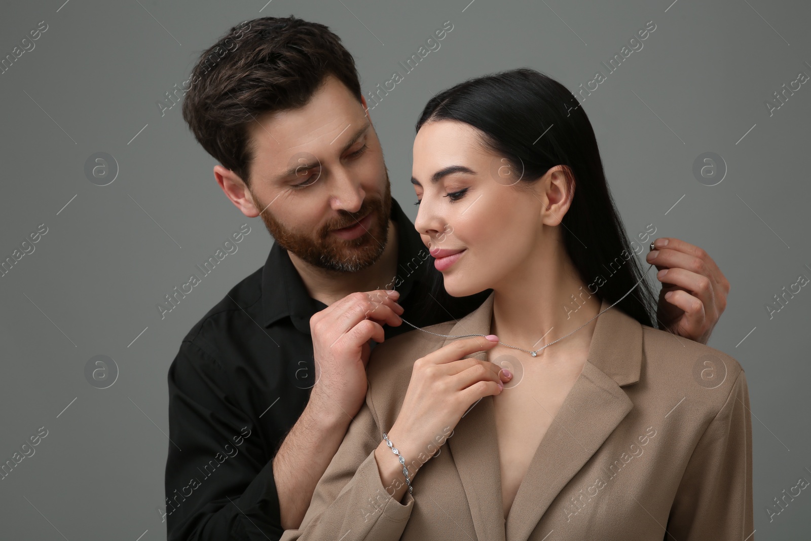 Photo of Man putting elegant necklace on beautiful woman against dark grey background