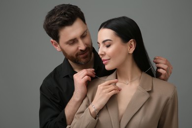 Photo of Man putting elegant necklace on beautiful woman against dark grey background