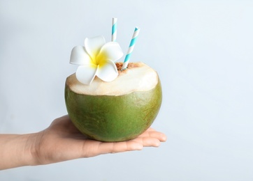 Female hand holding fresh green coconut with drinking straws on white background