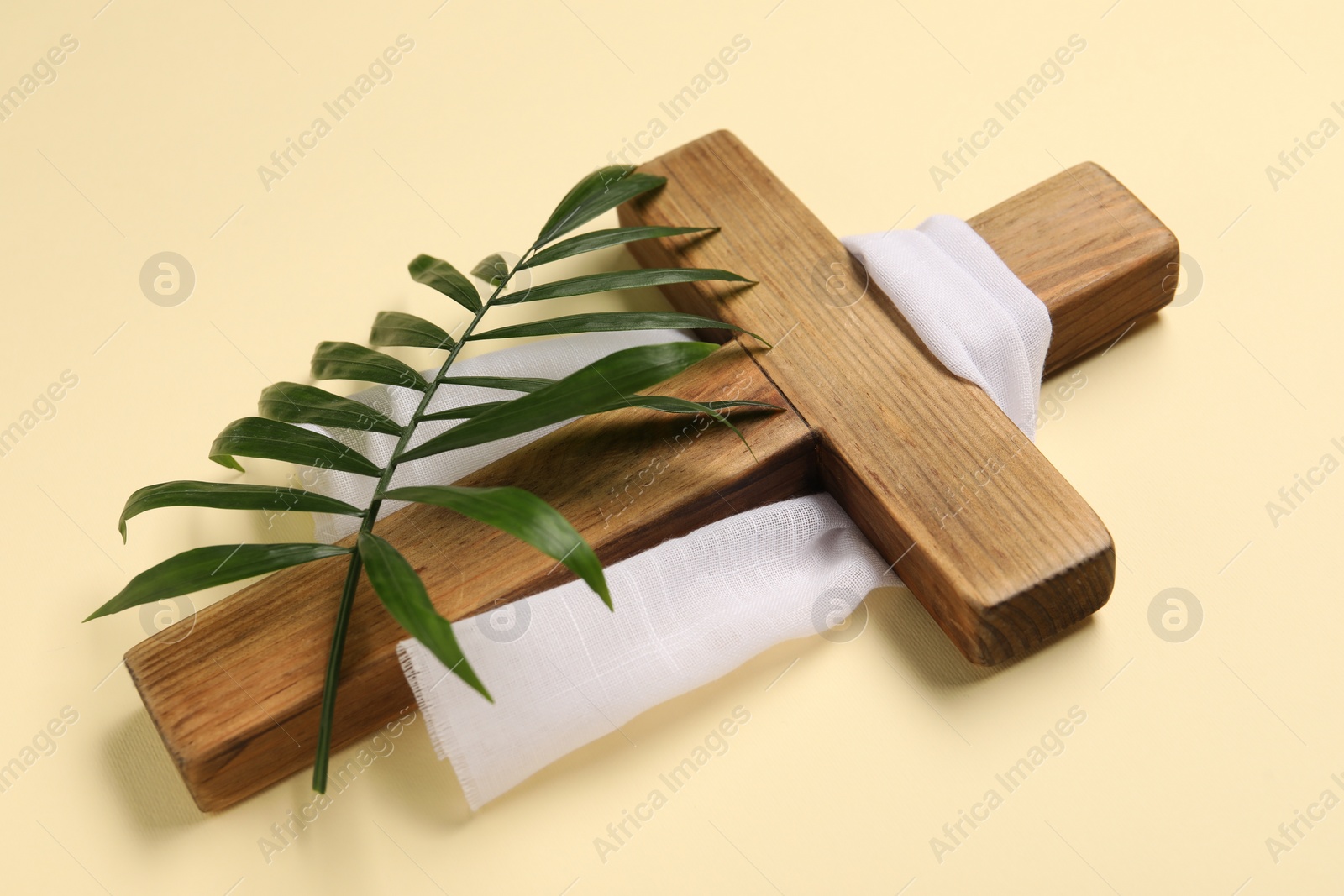 Photo of Wooden cross, white cloth and palm leaf on beige background. Easter attributes