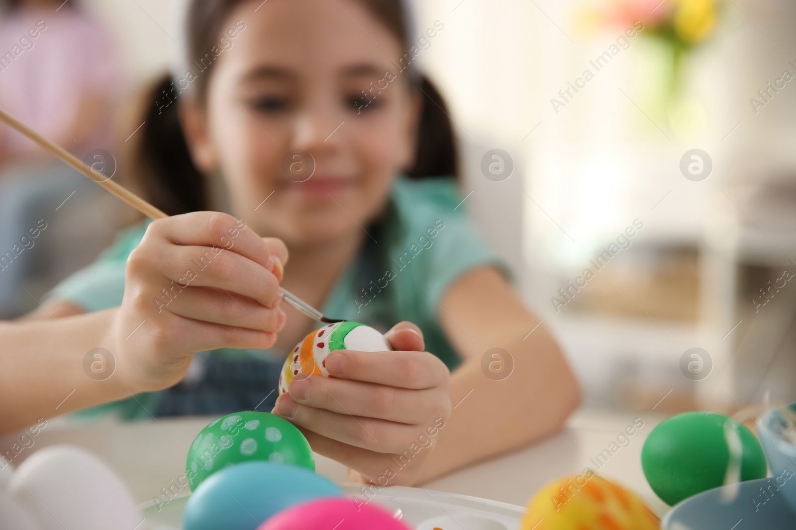 Photo of Little girl painting Easter eggs at table indoors, focus on hands