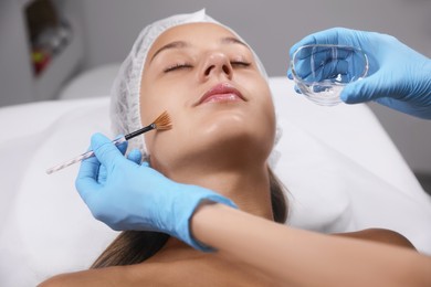 Cosmetologist applying chemical peel product on client's face in salon