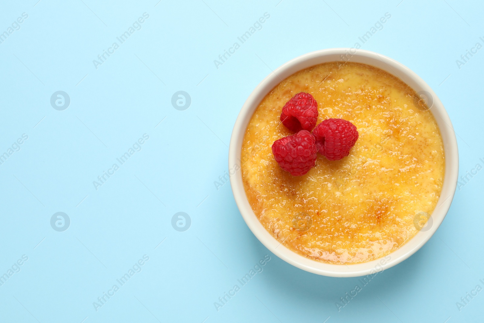 Photo of Delicious creme brulee with fresh raspberries on light blue background, top view. Space for text