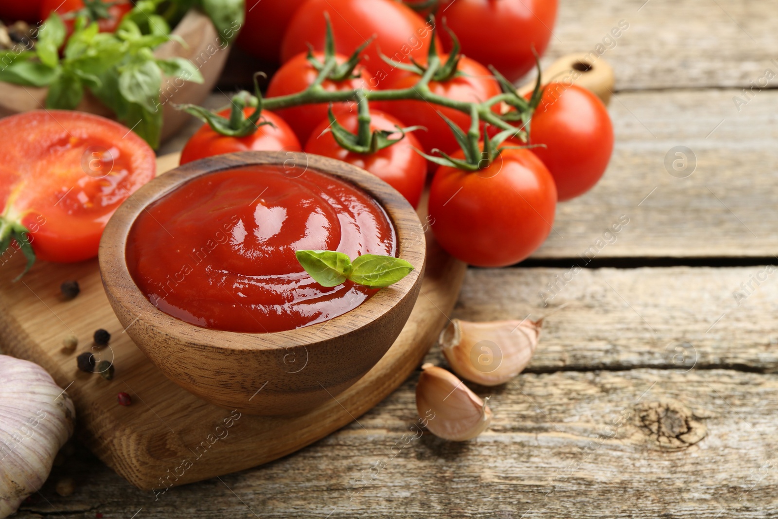 Photo of Tasty ketchup, fresh tomatoes, basil and spices on wooden table. Space for text