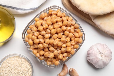 Photo of Delicious chickpeas and different products on white table, flat lay. Hummus ingredients