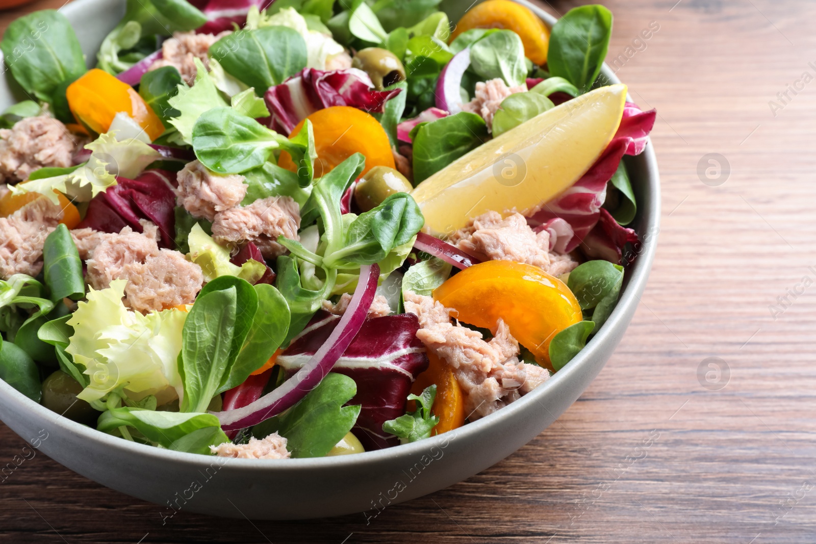 Photo of Bowl of delicious salad with canned tuna and vegetables on wooden table, closeup