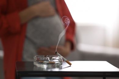 Cigarettes in ash tray and blurred pregnant woman on background, closeup. Space for text