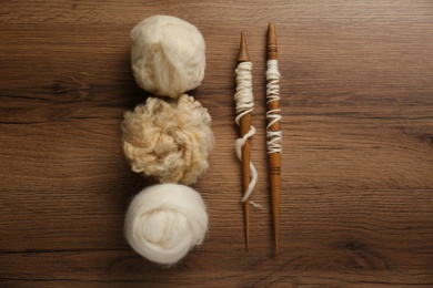 Photo of Soft white wool and spindles on wooden table, flat lay