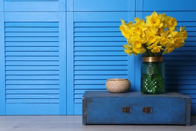 Photo of Vase with beautiful daffodils on wooden crate near light blue folding screen indoors, space for text
