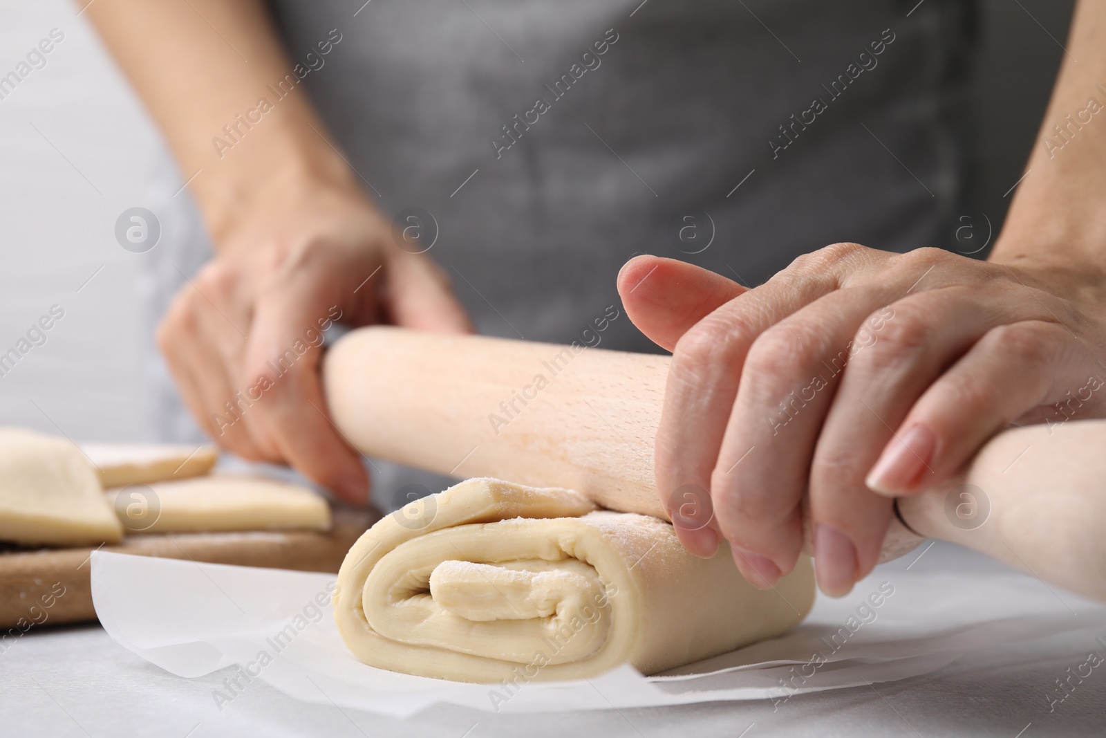 Photo of Woman rolling raw puff pastry dough at white table, closeup