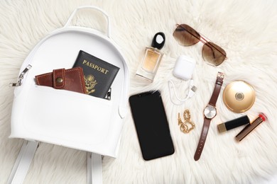 Photo of Stylish urban backpack and different items on white faux fur, flat lay
