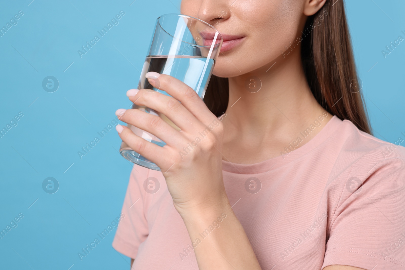 Photo of Healthy habit. Woman drinking fresh water from glass on light blue background, closeup