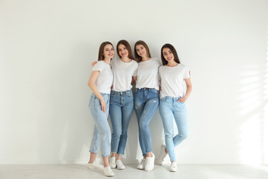 Beautiful young ladies in jeans and white t-shirts near light wall indoors. Woman's Day